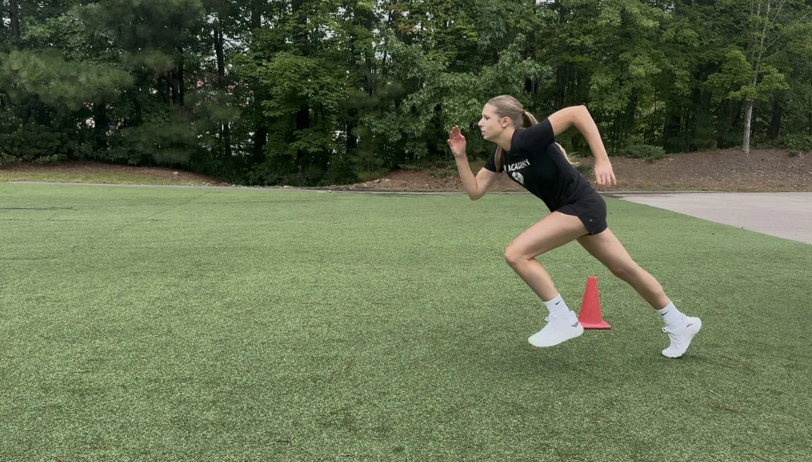 A volleyball athlete driving out of her first step past a cone on the turf